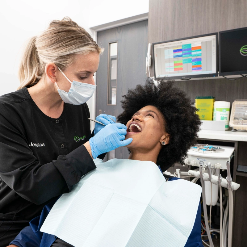 Female dentist examining patient's teeth in modern dental office treatment room.