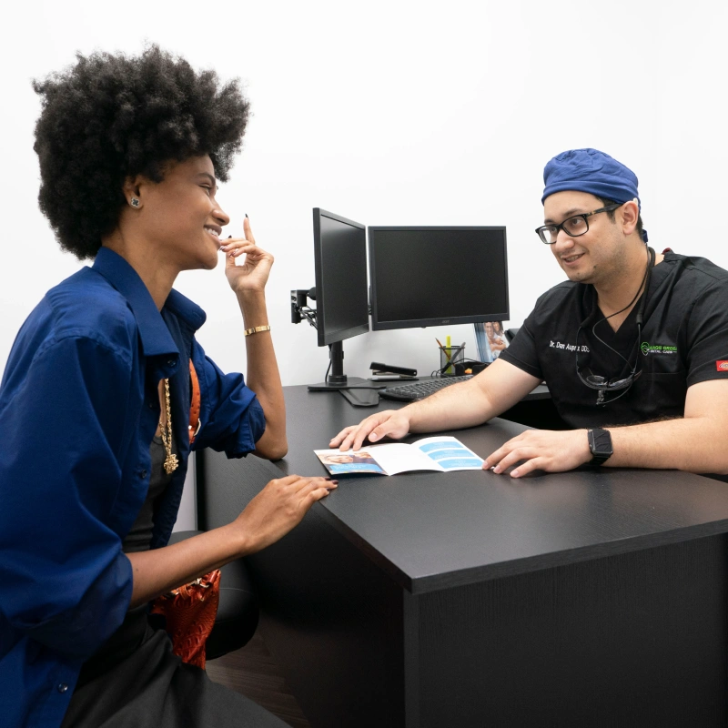 Dental consultation between patient and dentist reviewing treatment plans at office desk.