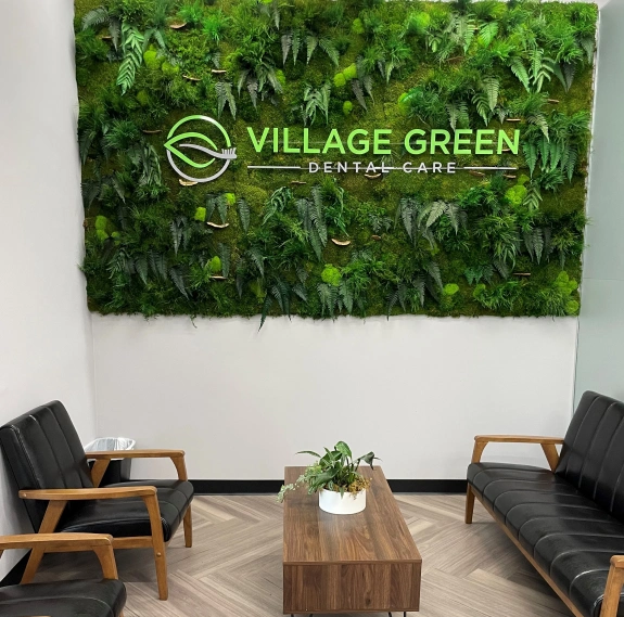 Village Green Dental Care logo on a living plant wall above modern seating.