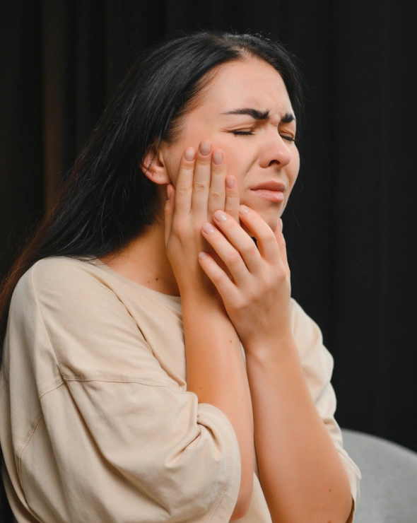 Woman holding her cheek in pain, illustrating dental emergency symptoms requiring urgent care.