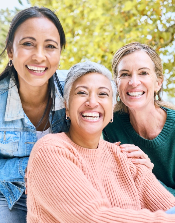 Three women smiling together outdoors in Kanata, representing dental patients and staff.