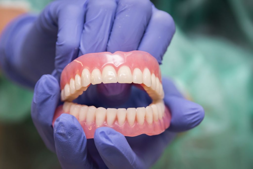 Denturist holding immediate dentures with gloves on