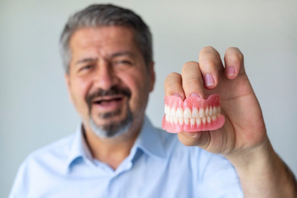 Elderly man holding a set of standard dentures